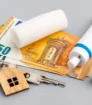Financiele elementen, zoals eurobiljetten en een houten sleutelhanger, gecombineerd met een rol verband en een tube creme, symboliseren de bijkomende kosten van tattoo weglaseren.