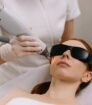 Vrouw ondergaat een laserbehandeling in het gezicht met professionele apparatuur, huidbescherming en veiligheidsbril.