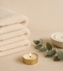 Minimalistische wellnessfoto met zachte opgerolde handdoeken, kaarsje en spa elementen in neutrale setting