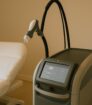 Moderne laserbehandelingsapparatuur in een esthetische kliniek met behandelstoel op de achtergrond.