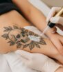 Professional verwijdert tattoo met saline techniek; witte zoutspray op zwart tattoo ontwerp op onderarm.